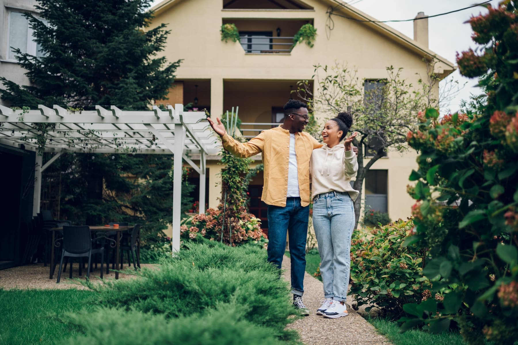 A couple arriving home through their front garden on a bright day.