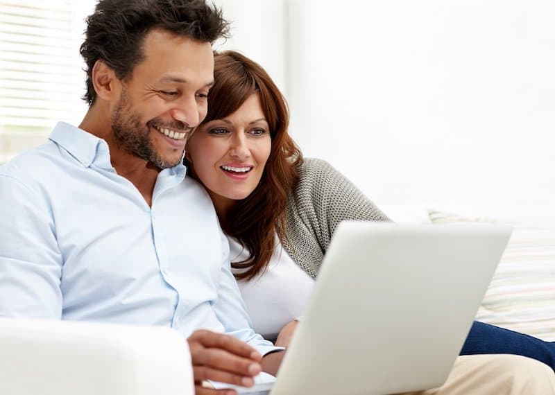 A couple on the sofa looking at the same laptop screen together.